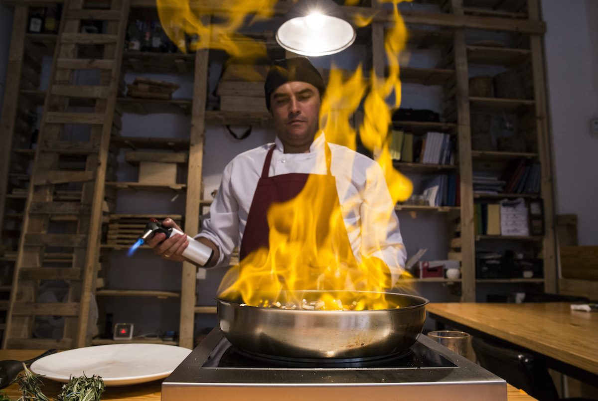 Man flambing beef cheeks with sauteed vegetables in a pan using a kitchen torch Cranky culture no excuse