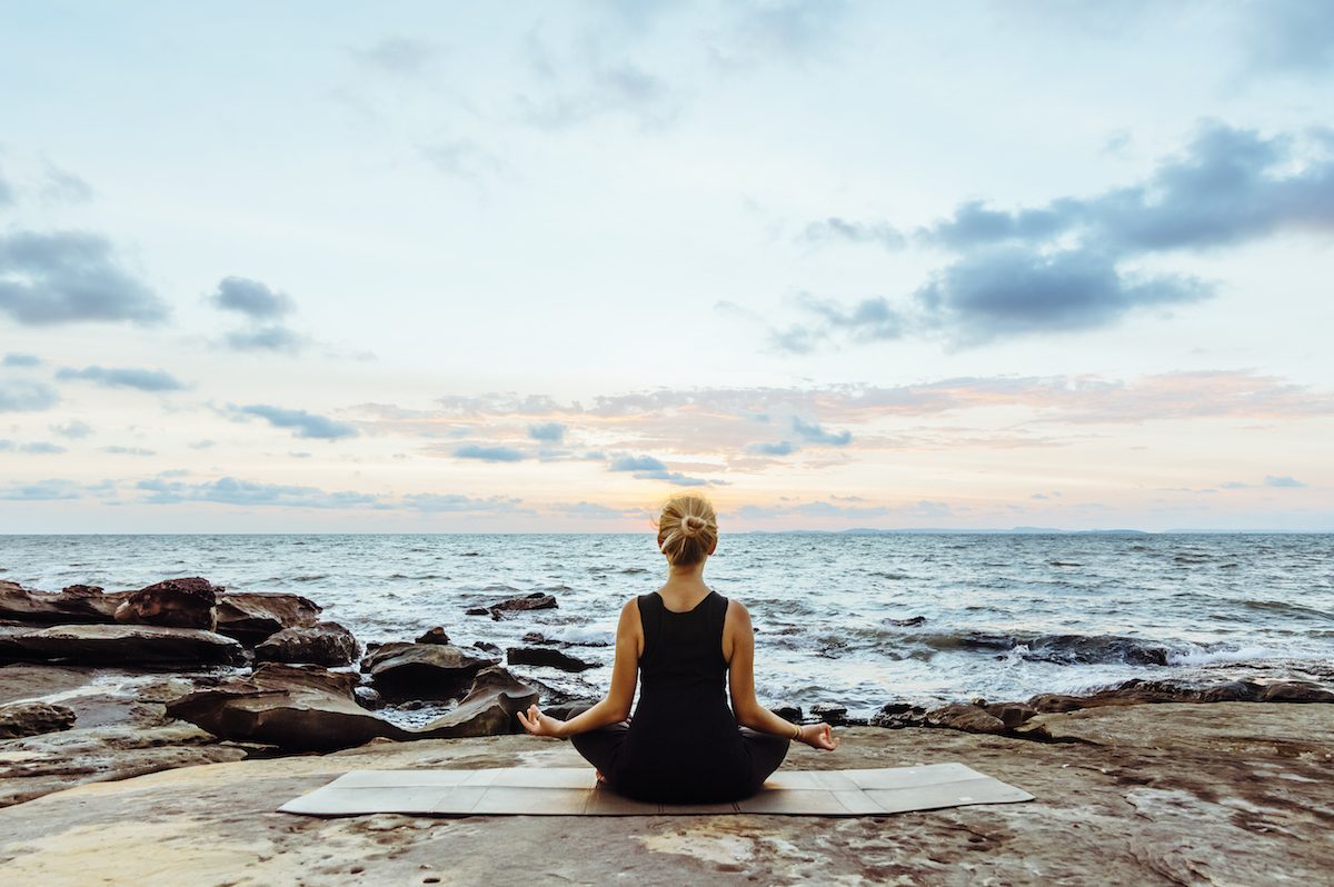 Young woman performs yoga moves on bluff above sea 4 ways to improve mental resilience