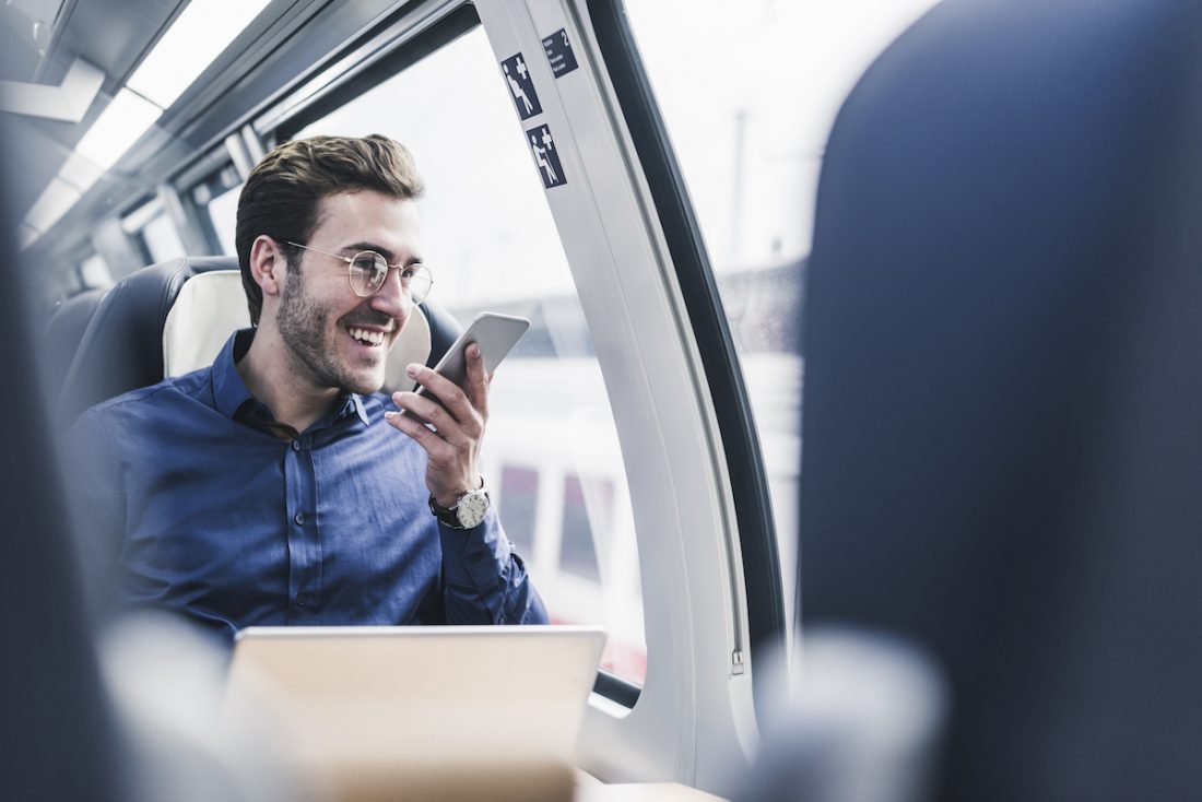 Happy businessman in train using cell phone Should your employees be paid to work as part of their commute?