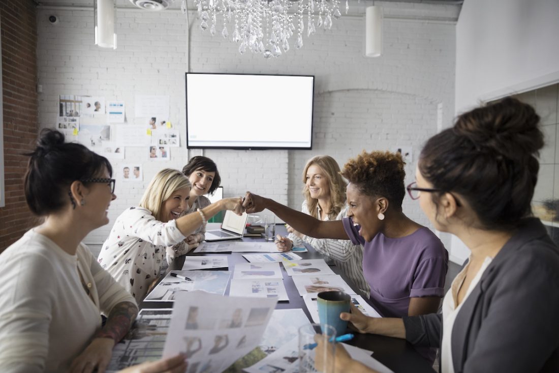 Female designers fist bumping in conference room meeting leader